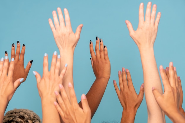 Photo mains d'un grand groupe de jeunes femmes de diverses ethnies à la peau blanche et foncée, levant les bras sur bleu