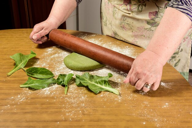 Mains de grand-mère pétrissant la pâte pour les nouilles dans la cuisine