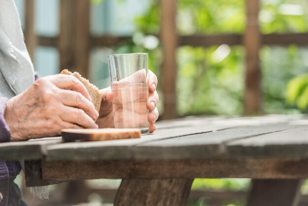 Les mains de la grand-mère tiennent un verre et du pain sur une table en bois