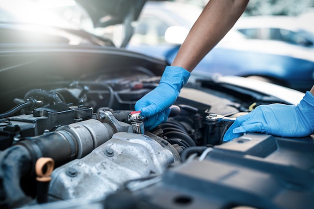 Mains en gros plan d'une jeune femme mécanicienne souriante effectuant des diagnostics sur une voiture