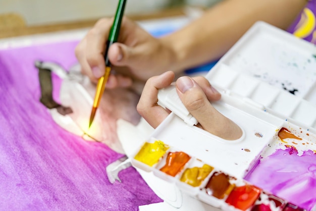 des mains en gros plan tenant un pinceau et une palette colorée avec des peintures à l'aquarelle par peinture d'artiste
