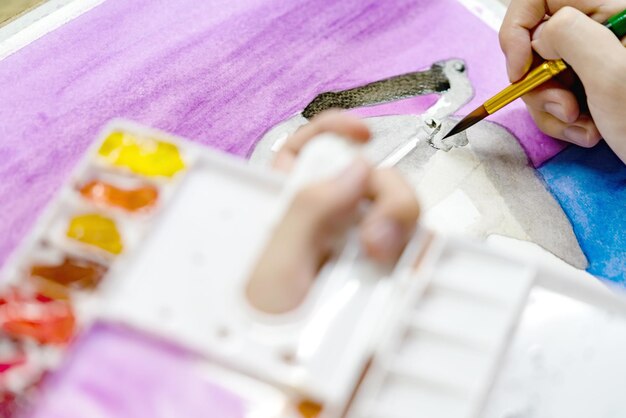 des mains en gros plan tenant un pinceau et une palette colorée avec des peintures à l'aquarelle par peinture d'artiste