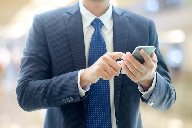 Mains d&#39;homme d&#39;affaires à l&#39;aide de téléphone intelligent sur le bureau de flou avec fond clair de bokeh