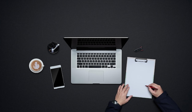 Mains d'homme d'affaires écrivant sur du papier blanc avec des fournitures de bureau. Mise à plat et vue de dessus avec espace de copie sur fond noir .concept de style de vie de bureau d'affaires.