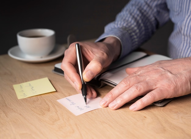 Mains d'homme d'affaires écrivant des notes de mémo ou un rappel sur un autocollant au bureau.