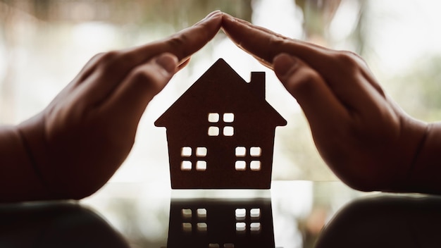 Les mains d'un homme d'affaires entourent un modèle de maison en bois