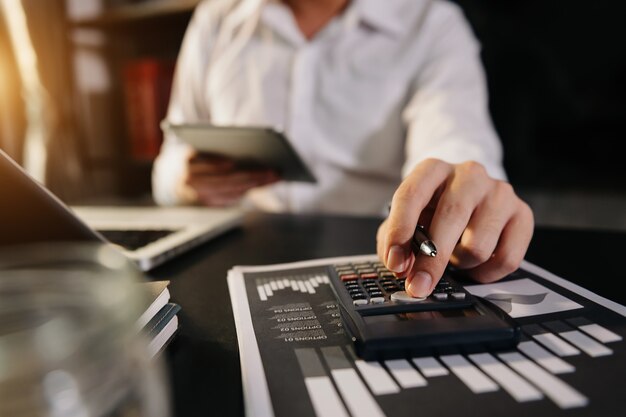 Mains d'homme d'affaires travaillant avec les finances sur le coût et la calculatrice et l'ordinateur portable avec tablette, smartphone au bureau à la lumière du matin