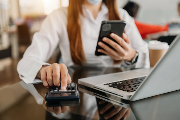 Mains d'homme d'affaires travaillant avec les finances sur le coût et la calculatrice et l'ordinateur portable avec tablette smartphone au bureau le matin lightxA