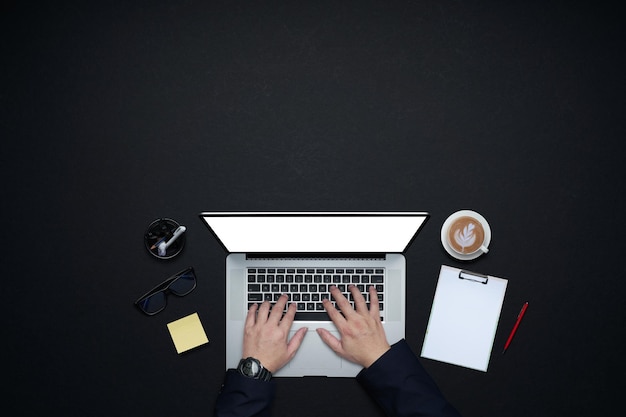 Mains d'homme d'affaires travaillant avec un ordinateur portable. Mise à plat et vue de dessus avec fournitures de bureau et espace de copie sur fond noir