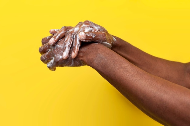 Les mains d'un homme afro-américain dans le savon et la mousse sur fond jaune le type se lave les mains