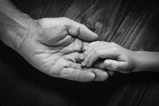 Mains d'un homme âgé tenant la main d'un homme plus jeune. Beaucoup de texture et de caractère dans les mains du vieil homme.