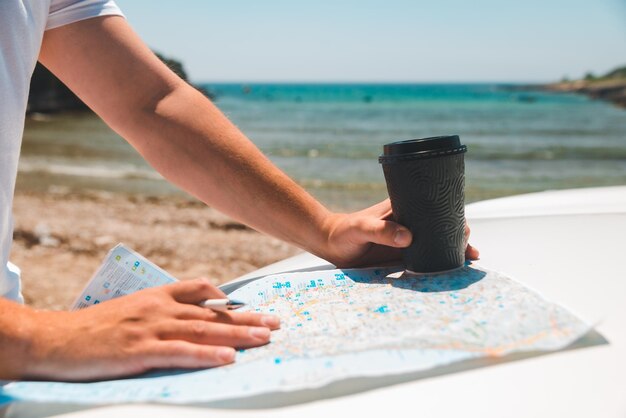 Mains d'homme sur la carte au capot de voiture tenant la tasse de café