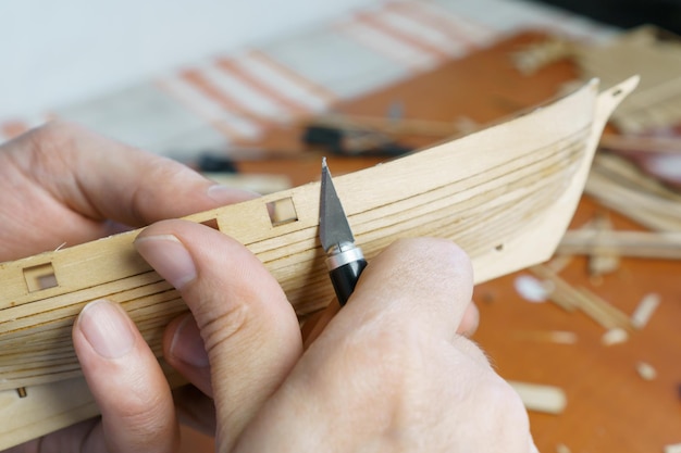 Mains homme coupant les détails du modèle de navire avec un couteau de bureau en contreplaqué Processus de construction d'artisanat de navire jouet