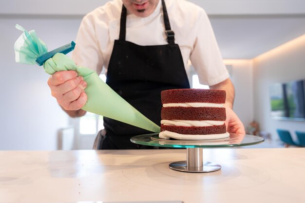 Mains d'un homme cuisinant un gâteau de velours rouge à la maison base de génoise triple avec la poche à douille assemblée nous commençons à couvrir les bords