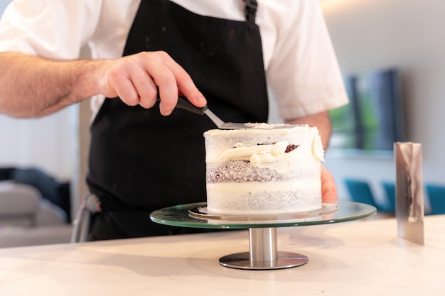 Mains d'un homme cuisinant un gâteau de velours rouge à la maison avec la spatule de lissage laissant le cercle parfait