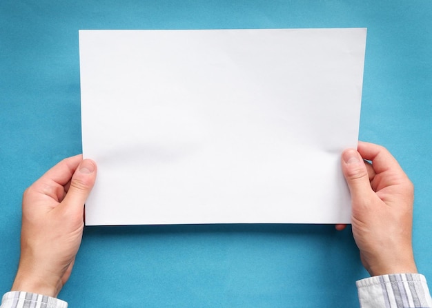 Mains d'un homme dans une chemise à carreaux tenant une feuille de papier blanc vierge sur fond bleu