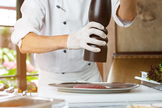 Les mains de l'homme avec un distributeur de poivre, un morceau de viande crue doivent ajouter du poivre. Le chef prépare du canard épicé ...