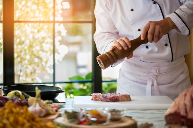 Les mains de l'homme avec distributeur de poivre. Viande crue sur tableau blanc. Ajoutez du piquant au bœuf. Filet mignon de qualité supérieure.