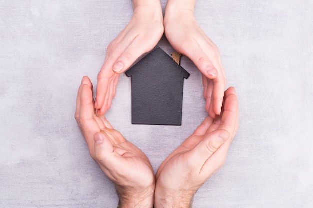 Mains d'homme et femme entourent un modèle d'une maison sombre sur fond gris