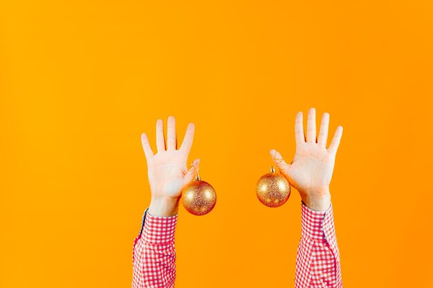 Mains d'un homme sur fond jaune, qui tiennent des jouets du Nouvel An, des boules de couleur dorée