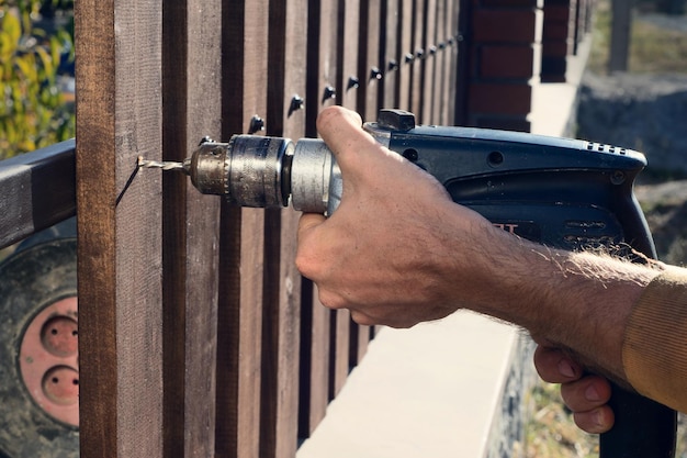 Mains d'homme forant une clôture en bois à la construction métallique Construire une clôture en bois avec une perceuse et une vis Gros plan de sa main et de l'outil dans un concept de bricolage