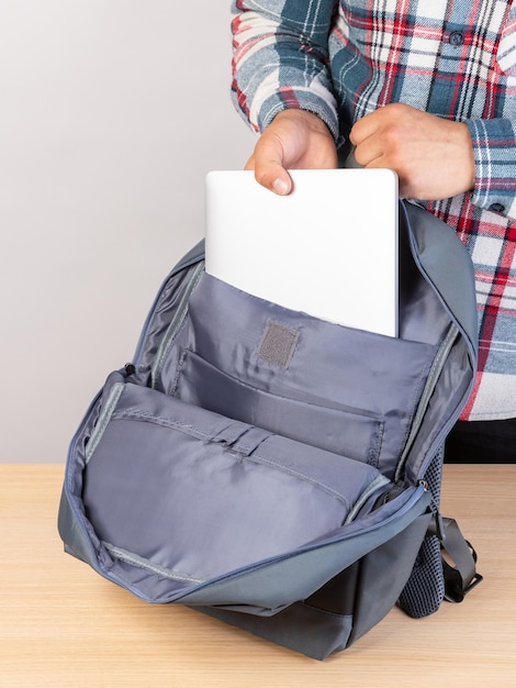 Les mains d'un homme incogniblement coupé dans une chemise à carreaux mis un ordinateur portable dans un sac à dos aller au travail