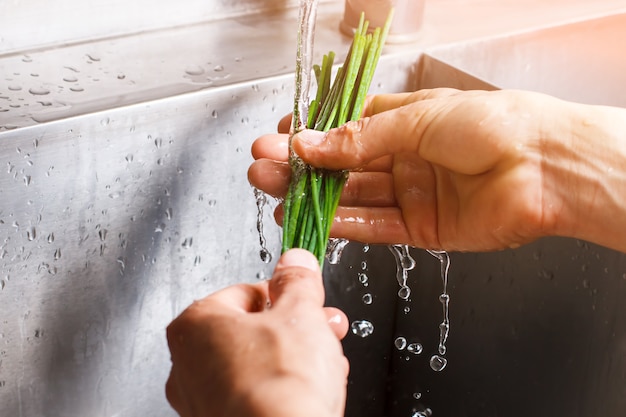 Les mains de l'homme lavent l'oignon vert. L'eau coule sur l'oignon vert. Herbes fraîches au goût épicé. Ingrédient clé de la salade végétarienne.