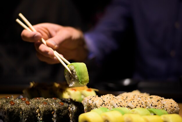 Photo mains d'homme manger des sushis avec des bâtons en bois