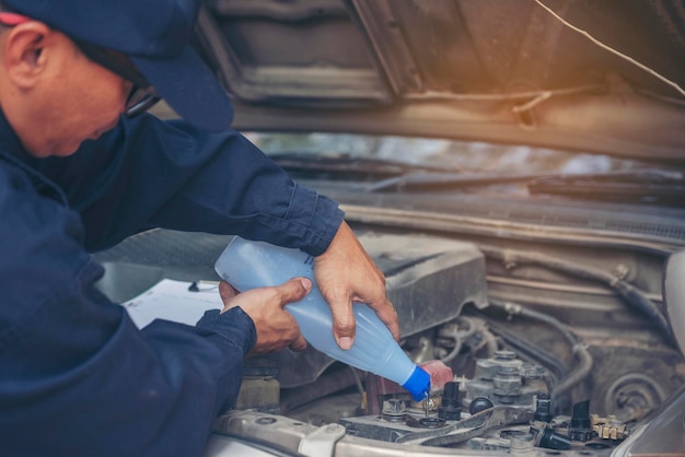 Mains d'homme mécanicien automobile versant de l'eau distillée purifiée déionisée pour le service mécanique de la batterie de voiture