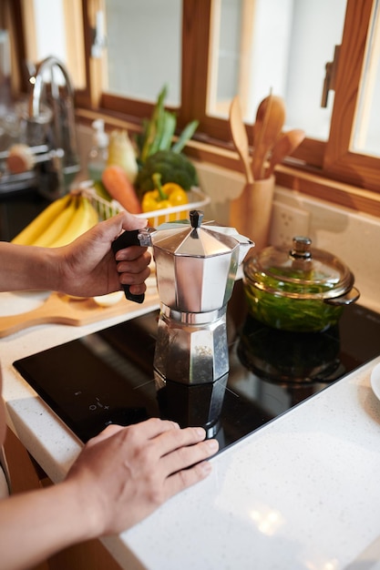 Mains d'homme mettant le pot de moka sur la cuisinière lors de la préparation du café du matin