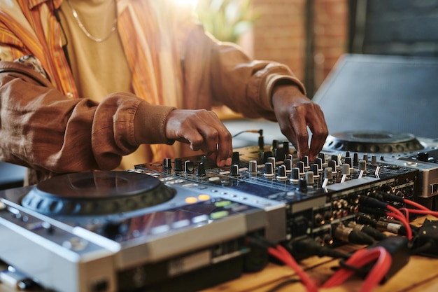 Mains d'homme noir réglant les sons sur le dj set tout en tournant les mélangeurs