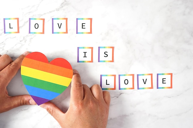 Mains d'un homme plaçant un coeur aux couleurs LGBTQ avec la phrase Love is Love sur un marbre