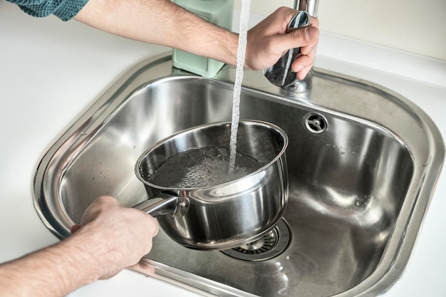 Les mains de l'homme remplissant une casserole en acier inoxydable avec de l'eau courante jusqu'à ce qu'elle bout et fasse cuire quelque chose