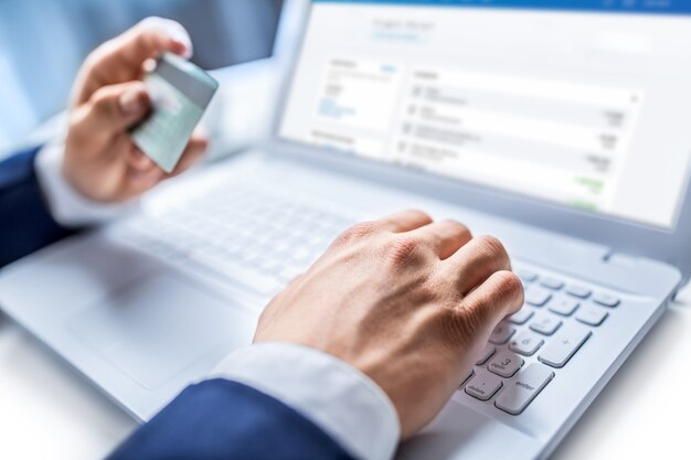 Mains d'homme tapant sur le clavier d'un ordinateur portable tenant une carte de crédit, gros plan sur des achats en ligne.