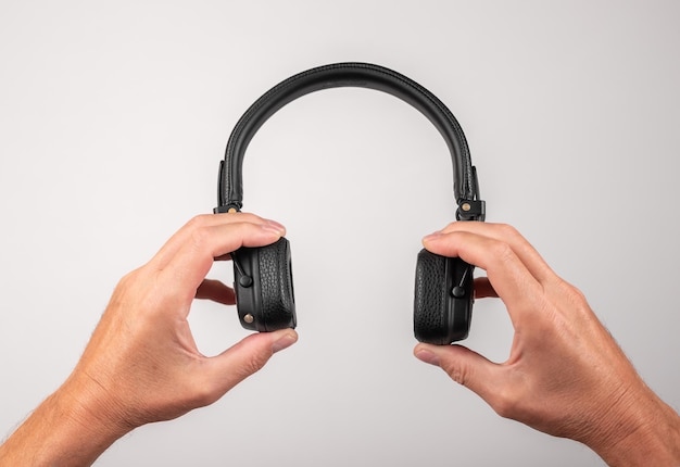 Mains d'homme tenant un casque Appareil électronique pour écouter de la musique podcasts livres audio et vidéos casque Relax concept sur fond gris