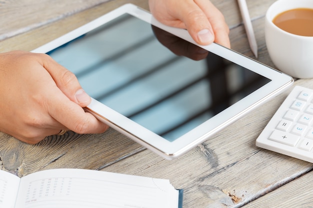 mains d'un homme tenant une tablette vierge sur une table d'espace de travail en bois