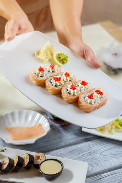 Les mains de l'homme tiennent une assiette de sushi. Wasabi sur tranche de citron. Rouleaux d'uramaki traditionnels au caviar. Plat japonais pour le petit déjeuner.