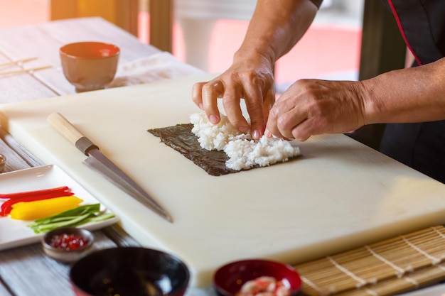 Les mains de l'homme touchant le riz blanc. Riz cuit sur feuille de nori. Recette originale de délicieux sushis. Ingrédients essentiels pour un plat japonais.