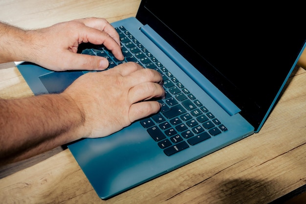 Mains d'un homme travaillant avec son ordinateur portable. Concept technologique, bureau à domicile