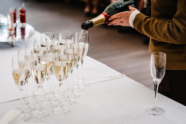 Mains d'homme versant du champagne à partir d'une bouteille en verre qui se tient sur une table blanche Gros plan L'homme remplit les verres de boissons d'élite debout sur trois rangées