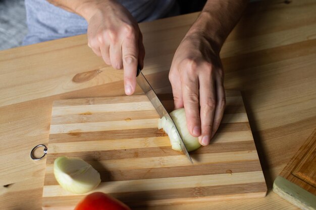 Les mains des hommes coupent les oignons sur une planche de bois