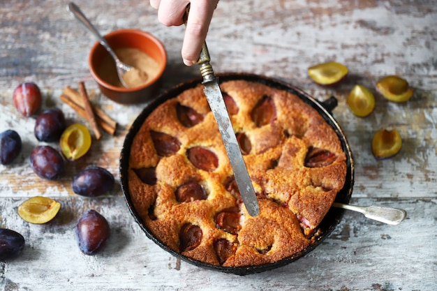 Les mains des hommes coupent la tarte aux prunes avec un couteau et une fourchette.