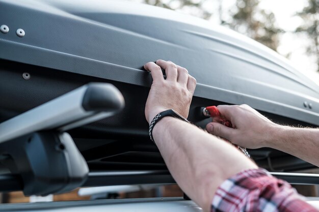 Les mains des hommes couvrent le coffre spacieux assemblé ou la boîte de chargement sur le toit de la voiture
