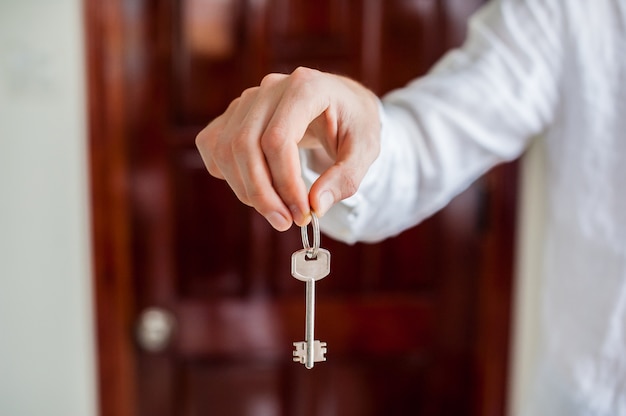 Les mains des hommes détiennent la clé de la maison sur un fond de porte en bois. Posséder un concept immobilier