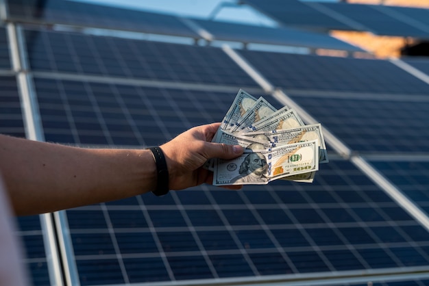 Les mains des hommes détiennent des dollars comme profit de la production d'énergie alternative. panneaux solaires