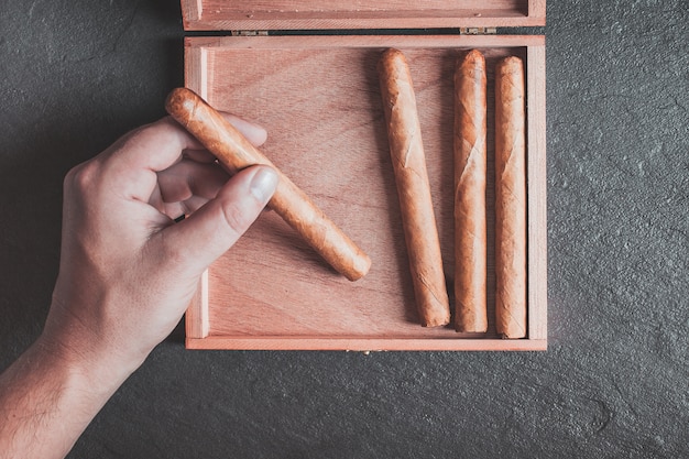 les mains des hommes sortent un cigare de la boîte sur une table sombre