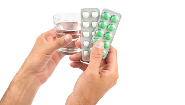 Les mains des hommes tiennent des assiettes de pilules blanches et vertes et un verre d'eau sur fond blanc