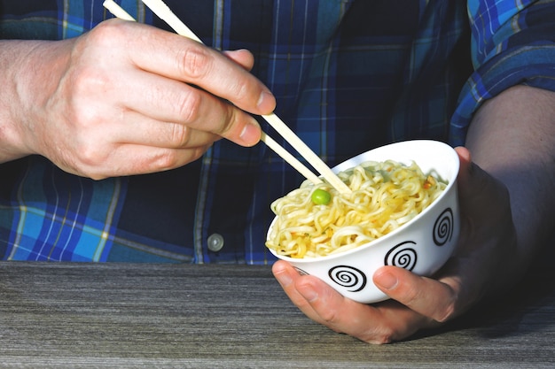 Les mains des hommes tiennent des nouilles avec des baguettes. Nouilles chinoises, bâtons, mains.