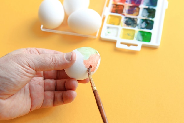 les mains des hommes tiennent un pinceau et peignent les œufs à l&#39;aquarelle.