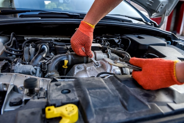 Mains humaines avec des clés dans des gants de protection sur le moteur de la voiture